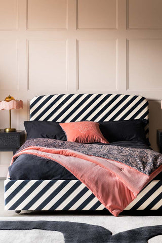The Jagger Bed in Studio Stripe Velvet Sand & Black styled with a pink cushion and throw, bedside tables and a lamp.