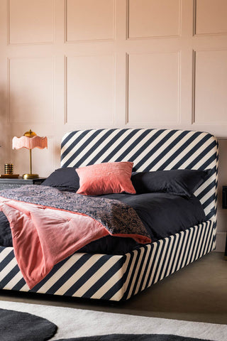 The Jagger Bed in Studio Stripe Velvet Sand & Black seen from an angle, styled with a pink cushion and throw on.
