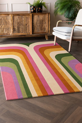 A styled image of the The Romy Retro Rug in Pink next to a wooden leopard print side board.