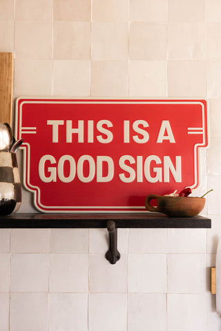 Red sign with 'This is a good sign' text on a white tiled wall.