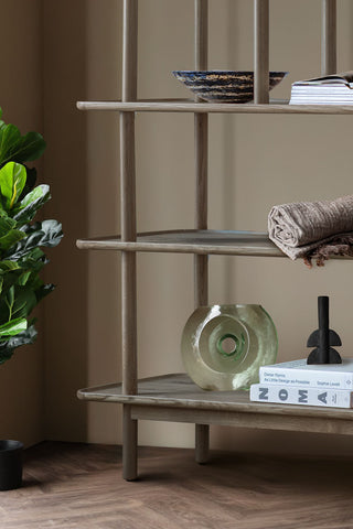 Close-up of the base of the Tiered Oak Display Cabinet In Grey styled with various home accessories on next to a plant.