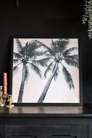 Lifestyle image of Vintage Pink Palms 50cm x 50cm Art Print in a black frame on a dark background.