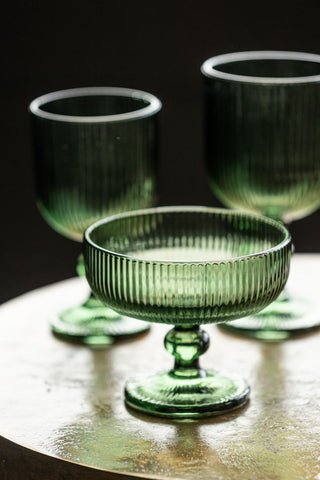 The Vintage Style Champagne Glass - Green displayed on a table, with two green wine glasses in the background.