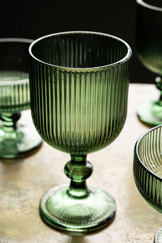 The Vintage Style Red Wine Glass - Green on a table, surrounded by other glasses.