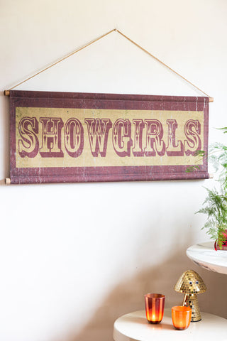 The Vintage-Style Showgirls Wall Art styled on a light coloured wall next to a white sideboard, styled with a plant, candle and mushroom.