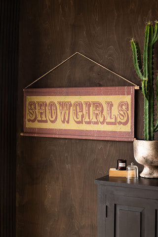 The Vintage-Style Showgirls Wall Art styled on a dark brown wall next to a black sideboard, styled with a cactus, candle and book.