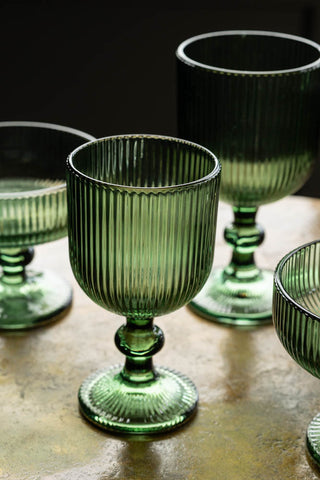 The Vintage Style White Wine Glass - Green displayed on a table with other green glassware.