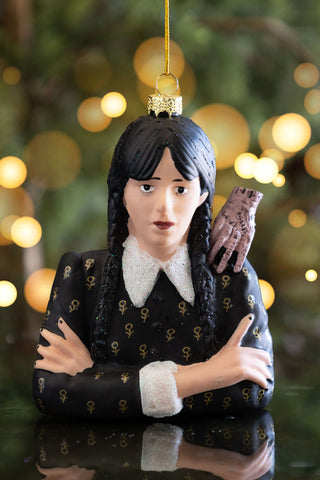 Ornament of a character with dark hair and a black outfit with gold patterns, held against a blurred Christmas tree background.