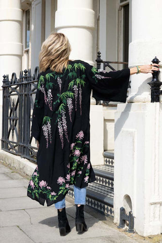 The Long Wisteria & Chrysanthemums Black Kimono worn by a model in front of a building.