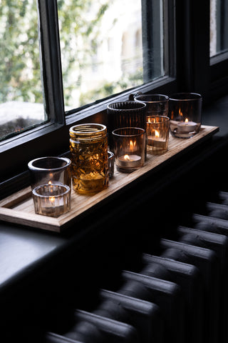 Moody interior shot of the amber glass votives on a wooden board styled on a windowsill.