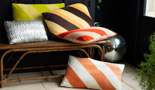 Lifestyle image of the new HKliving cushions styled on a wicker bench, with a disco ball and plant also in the shot. 