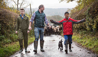 Image of a farmer, two happy  kids, a dog and a heard of  cows on a country lane. 