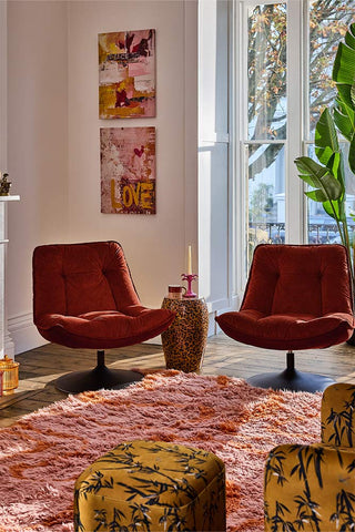 Two burnt orange armchairs in a living room with colourful rugs, artwork and armchairs.