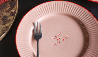 One of the Set of 4 Pink & Red First Bite Side Plates displayed on a black table with other kitchen accessories.