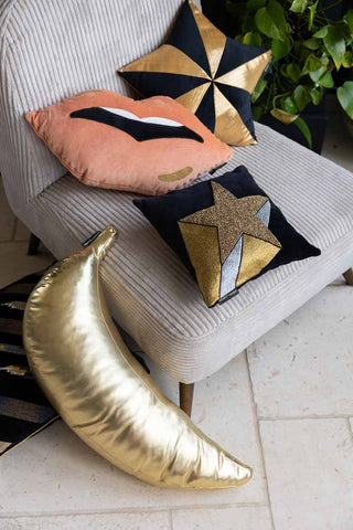 Lifestyle image of the Gold Banana Cushion styled with other cushions on an armchair.