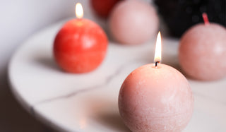 The Unique Ball Candle In Misty Pink displayed lit on a marble table, with other candles in the background.
