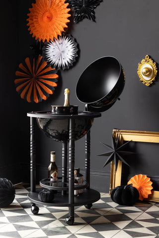 Decorative Halloween setup with black globe bar, bottles, and festive decorations on a checkered floor.