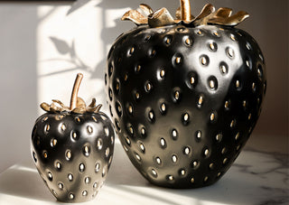Lifestyle image of the Small and Large Black & Gold Strawberry Ornaments displayed together on a table in the sunshine. 
