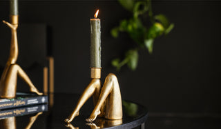 The Sexy Gold Legs Candle Holder with a lit candle inside, displayed on a black table with the Kick Gold Leg Candle Holder in the background.