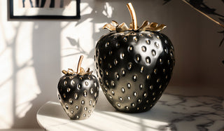 The Small/Large Black & Gold Strawberry Ornaments displayed together on a table in the sunshine.