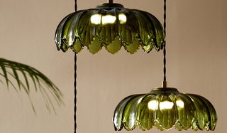 The Gold & Green Cluster Desert Island Palm Light in front of a neutral wall and plant.