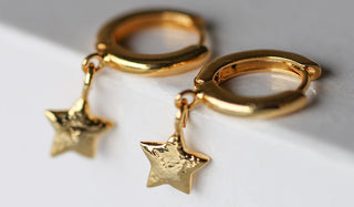 The You're A Star Gold Huggie Hoop Earrings displayed together draped over a white surface. 