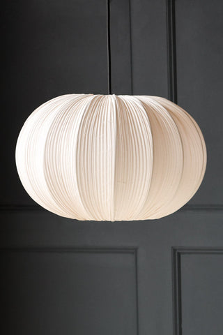 The Neutral Pleated Fabric Ceiling Light, hanging from a black cord, against a dark grey wall