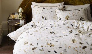 Lifestyle image of the Jane's Rose Duvet Cover and Pillow Case Set styled on a bed with a velvet headboard next to a bedside table with items on.