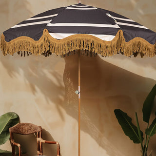 The HKliving Stripe Parasol displayed with a chair and plants in front of a neutral wall.