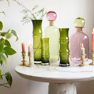 The Small, Medium and Large Green Glass Bamboo Vases, arranged with the Small and Large Pink & Green Apothecary Bottles and gold candlesticks with lit candles on a white marble table.