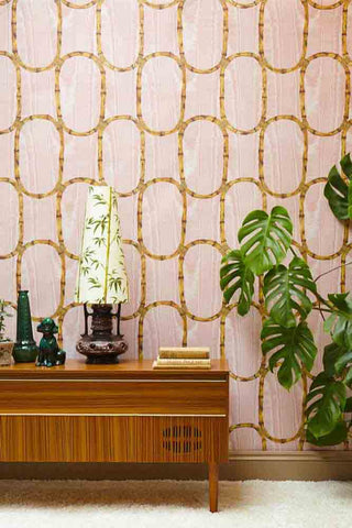 A room with pink and bamboo patterned wallpaper, a wooden console table and large plant.