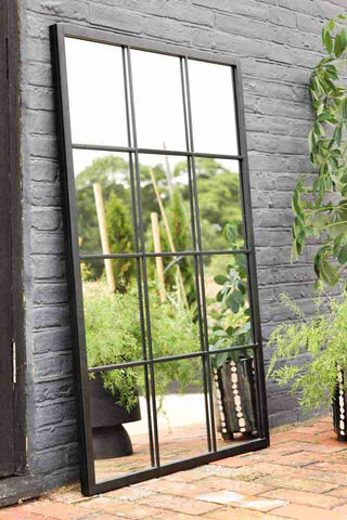 Large black mirror with window pane style grid, photographed outside in a garden. 