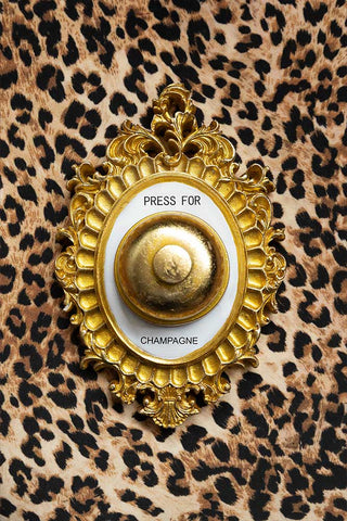 Decorative gold bell with 'Press for Champagne' text on a leopard print background