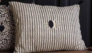The Monochrome Eclipsed Sun Cotton Cushion displayed on a wicker bench.