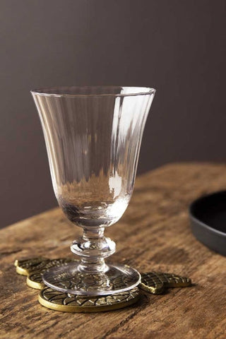 Lifestyle image of the Ribbed Glass Wine Glass on a coaster on wooden surface with dark wall background