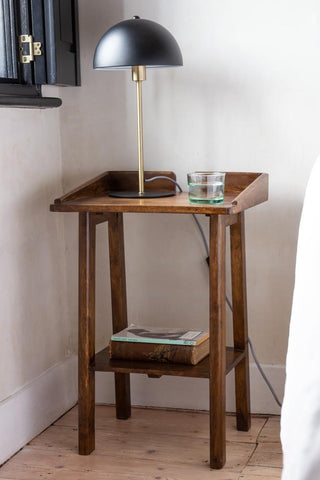 Lifestyle image of the Dark Mango Wood Bedside Table With Cable Gap with books on the bottom shelf