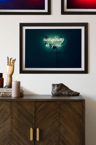 lifestyle Image of the Framed Everything Is Great Neon Art Print on white wall with wooden sidetable