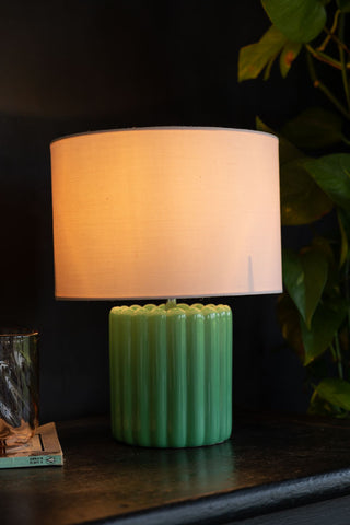 Lifestyle image of the Pretty Green & Pink Table Lamp on a black surface showing the light on 
