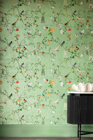 Image of light patterned wallpaper with birds, branches and flowers, displayed on wall behind a black table with decorative dish.