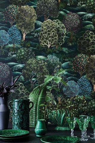 Lifestyle image of botanical wallpaper, a mix of beautiful foliage and an array of green glassware and pottery.