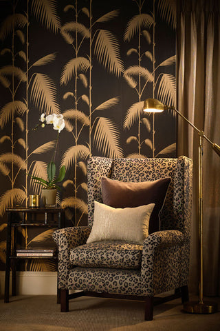 lifestyle image of cole & son new contemporary - palm leaves wallpaper - black & gold with leopard print armchair and gold floor lamp