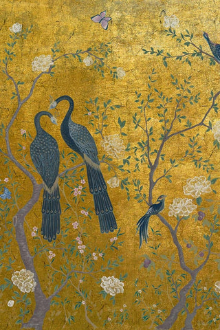 A close up image of wallpaper depicting two birds sitting in a floral tree on a gold background. 