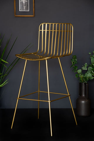 side angle lifestyle image of the midas bar stool with plants and black flooring and copper picture frame on dark wall background