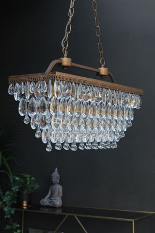 lifestyle image of stunning crystal droplets chandelier over black and gold console table with buddha ornament on with dark wall background