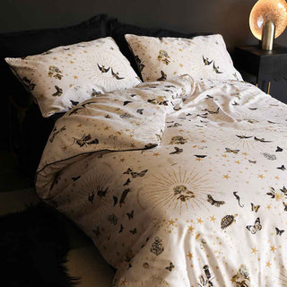 A double bed made with four pillows, two black and two with starbursts, swallows, stars and motifs on them, plus a duvet with the same motifs