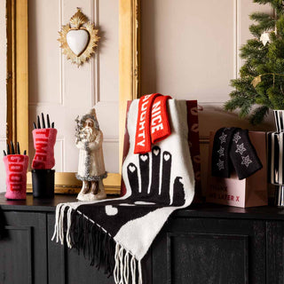 A selection of Christmas gifts styled on a sideboard including cosy scarves, hand warmers and a Christmas tree in the corner. 