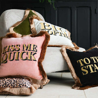 A pile of colourful and fringed cushions styled on a neutral armchair