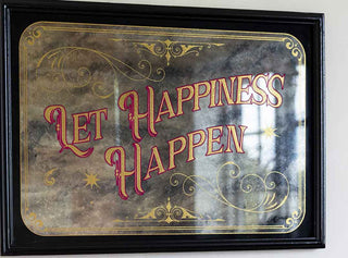 A foxed antique-style mirror with the words 'Let Happiness Happen' written on it 