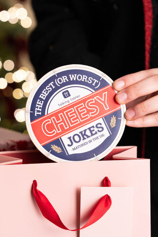 A game called Cheesy Jokes being placed into a pink gift bag. 