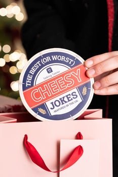 A game called Cheesy Jokes being placed into a pink gift bag. 